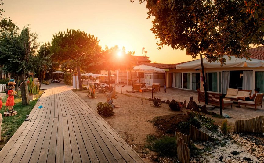 Tramonto su un sentiero di legno e case con giardino e sculture
