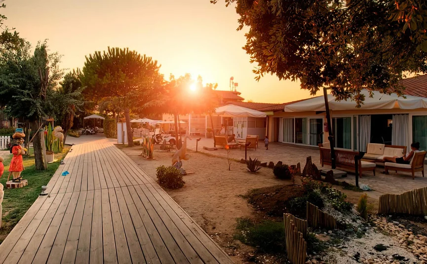 Sonnenuntergang über einem Holzweg und Häusern mit Garten und Skulpturen