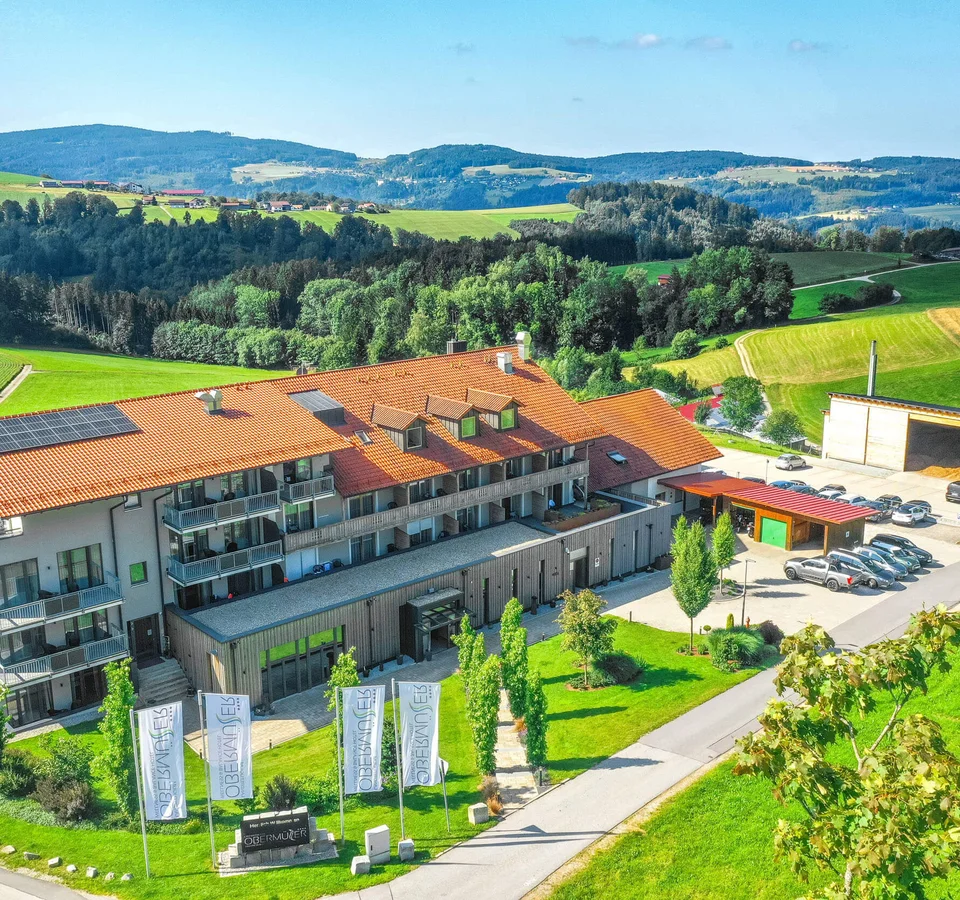 Modernes Gebäude mit rotem Dach und Autos in grüner Hügellandschaft