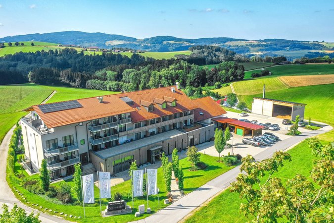 Modernes Gebäude mit rotem Dach und Autos in grüner Hügellandschaft