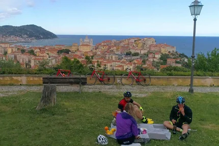 Drie fietsers picknicken met uitzicht op zee en kleurrijke stad