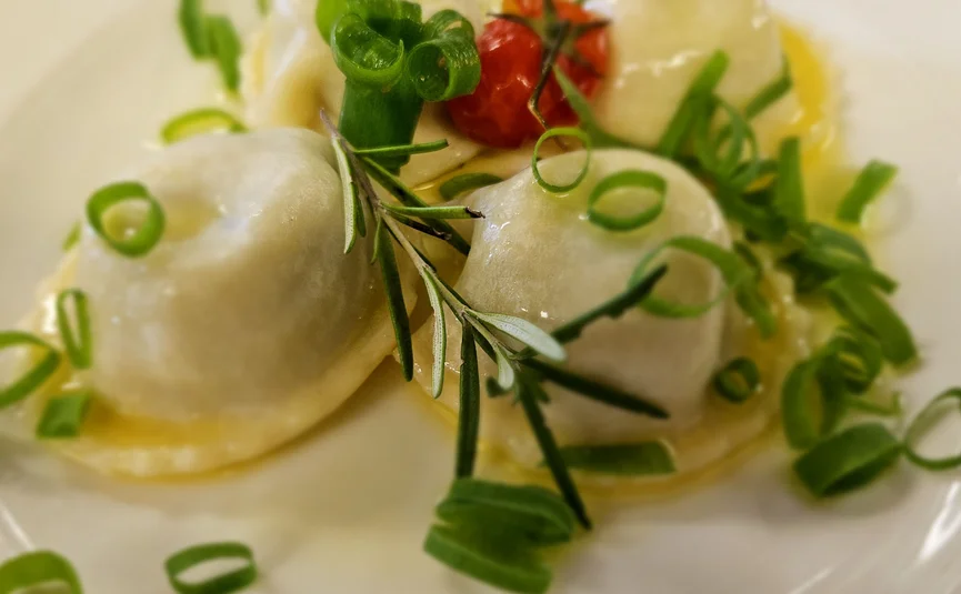 Teller mit gefüllten Ravioli, Frühlingszwiebeln und Tomate