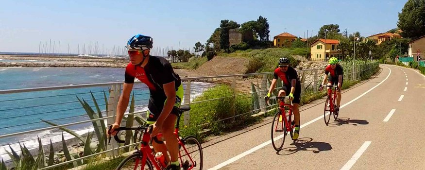 Tre ciclisti pedalano su una pista ciclabile costiera soleggiata