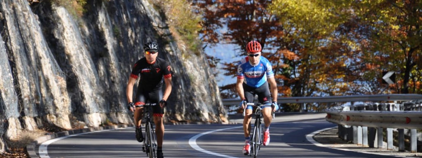 Two cyclists riding on a winding road through autumn forest