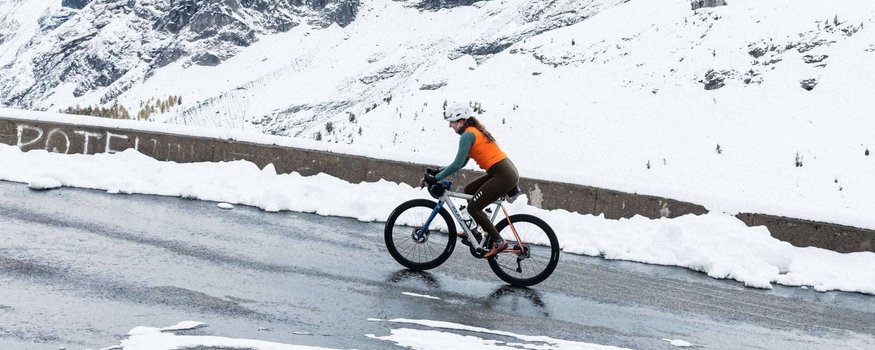 Fahrradfahrer auf verschneiter Bergstraße vor schneebedecktem Berg