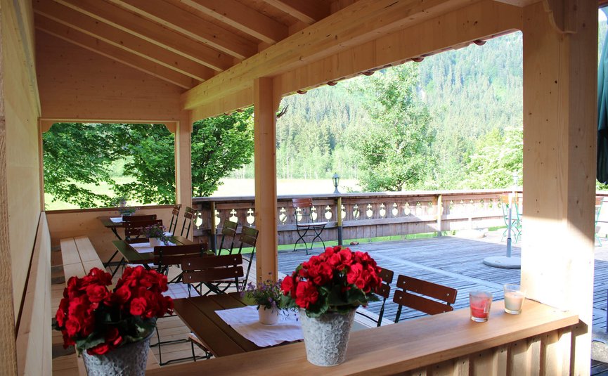 Überdachte Terrasse mit Holzmöbeln und Blumendekoration vor Waldkulisse