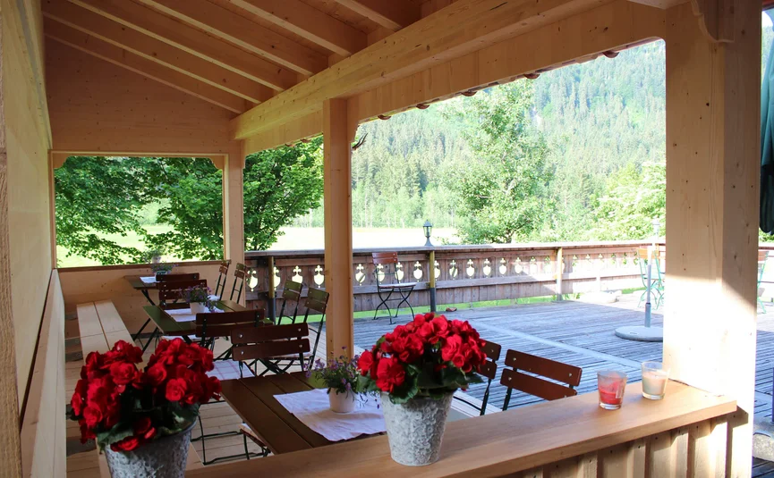 Gämsle Hotel, Wirtshaus & mehr .. © Raffael F. Lehner Covered wooden terrace with tables, chairs, and flower pots overlooking forest