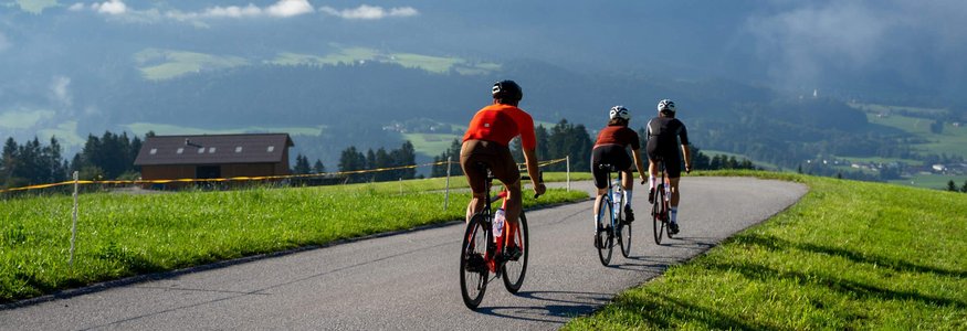 Drei Radfahrer fahren auf einer Landstraße mit Bergen und grüner Landschaft