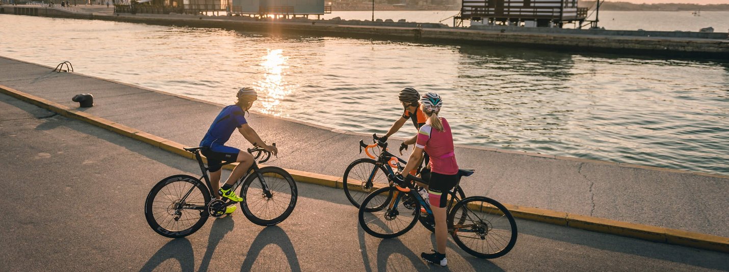 Drei Radfahrer stehen bei Sonnenuntergang an einem Wasserweg