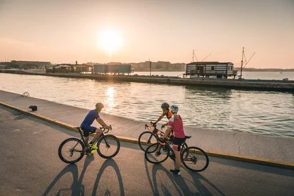 Drei Radfahrer stehen bei Sonnenuntergang an einem Wasserweg