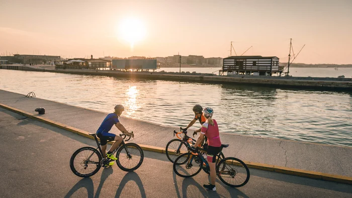 Drie fietsers stoppen bij water bij zonsondergang met gebouwen op de achtergrond
