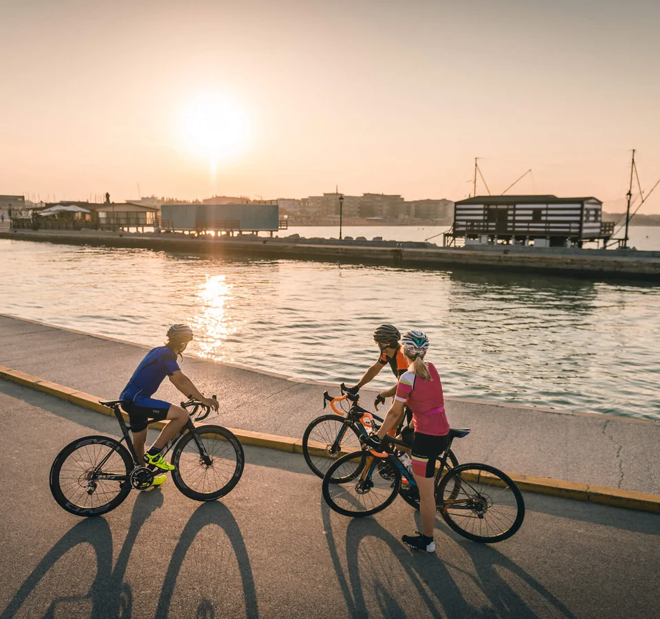 Adriatische Küste: Rennradurlaub mit Dolce Vita © Alex Moling Drei Radfahrer stehen bei Sonnenuntergang an einem Wasserweg