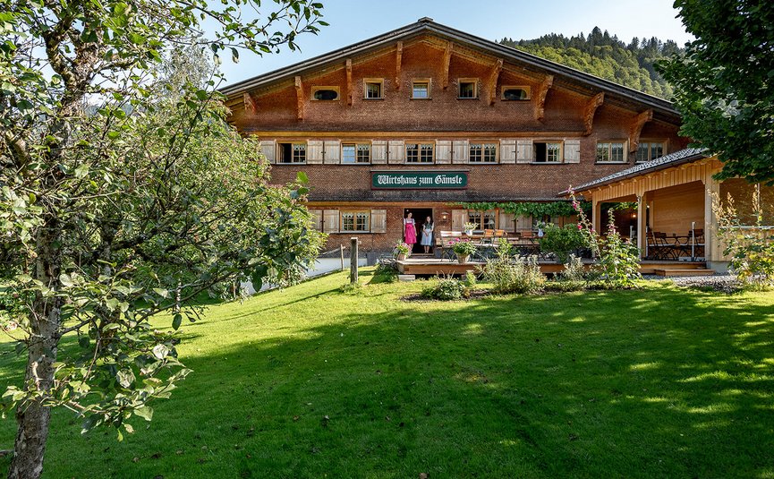 Traditionelles Gasthaus mit grüner Wiese und Obstbäumen im Vordergrund