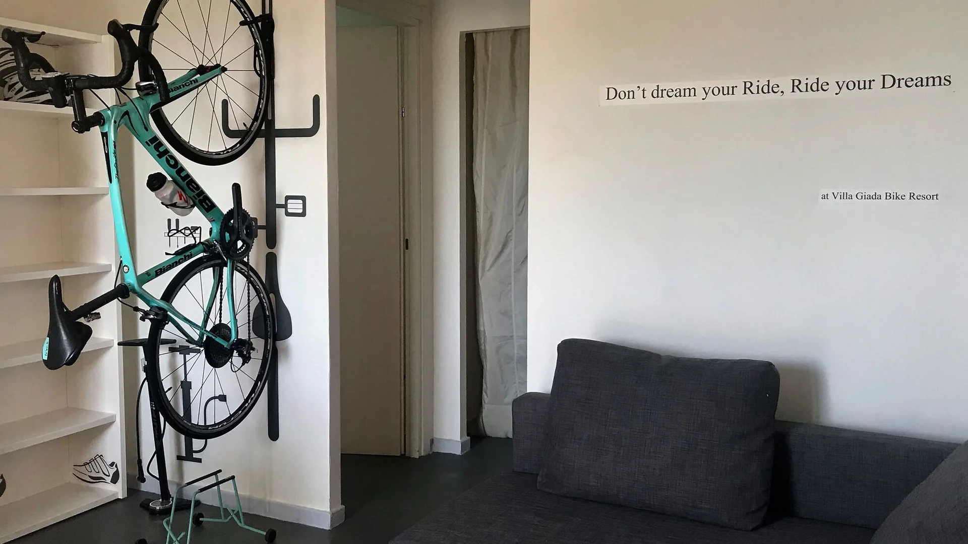 Villa Giada SpEace Resort: Mit deinem Rennrad aufs Zimmer © Villa Giada spEace Resort Fahrrad an der Wandhalterung neben grauem Sofa und Zitat an der Wand