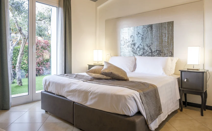 Modern bedroom with large bed and garden view through glass door