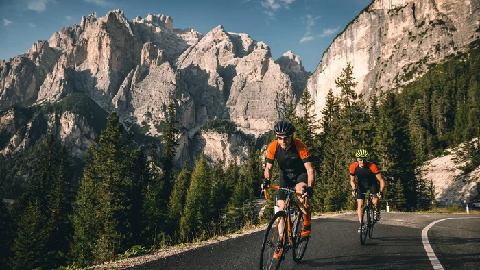 Giro d’Italia hautnah im Hotel Gran Paradiso © Molography Zwei Radfahrer fahren auf Bergstraße mit Felsen und Nadelbäumen im Hintergrund