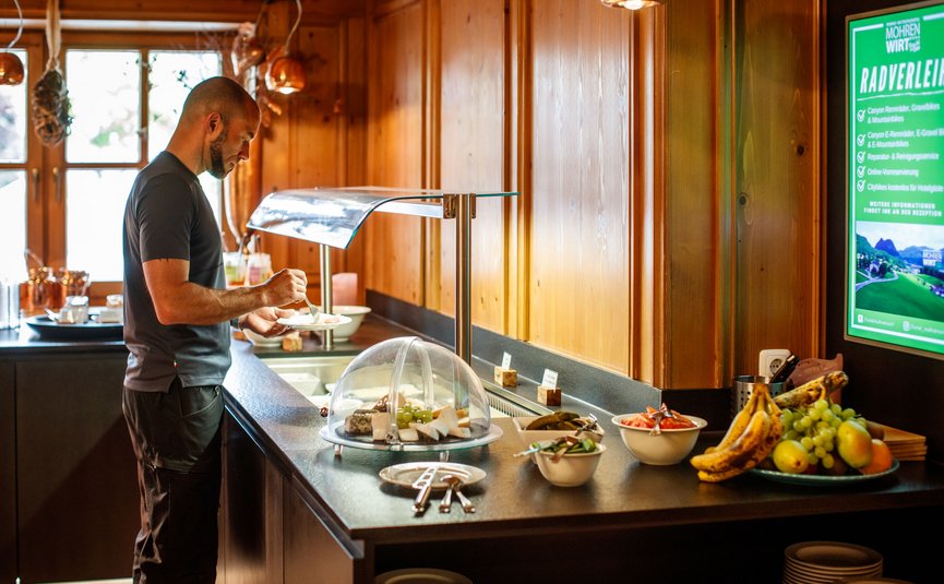 Man serving himself fruit and cheese at a buffet in a wooden room