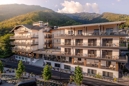 Modern hotel building with balconies set against forested mountains at sunset