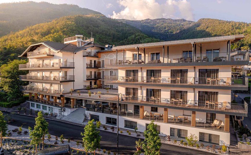 Edificio moderno di un hotel con balconi davanti a montagne boscose al tramonto