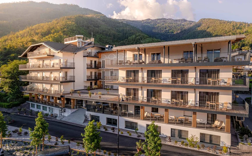 Cristallo Sport & Wellness Hotel **** © Andrea Acler Modernes Hotelgebäude mit Balkonen vor bewaldeten Bergen bei Sonnenlicht
