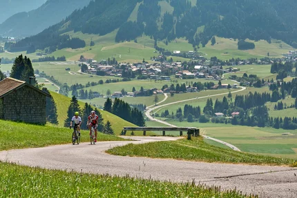 Zwei Radfahrer auf Bergstraße mit Tal und Bergen im Hintergrund