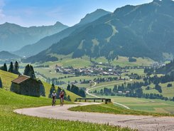 Due ciclisti su strada di montagna con vallata e montagne sullo sfondo