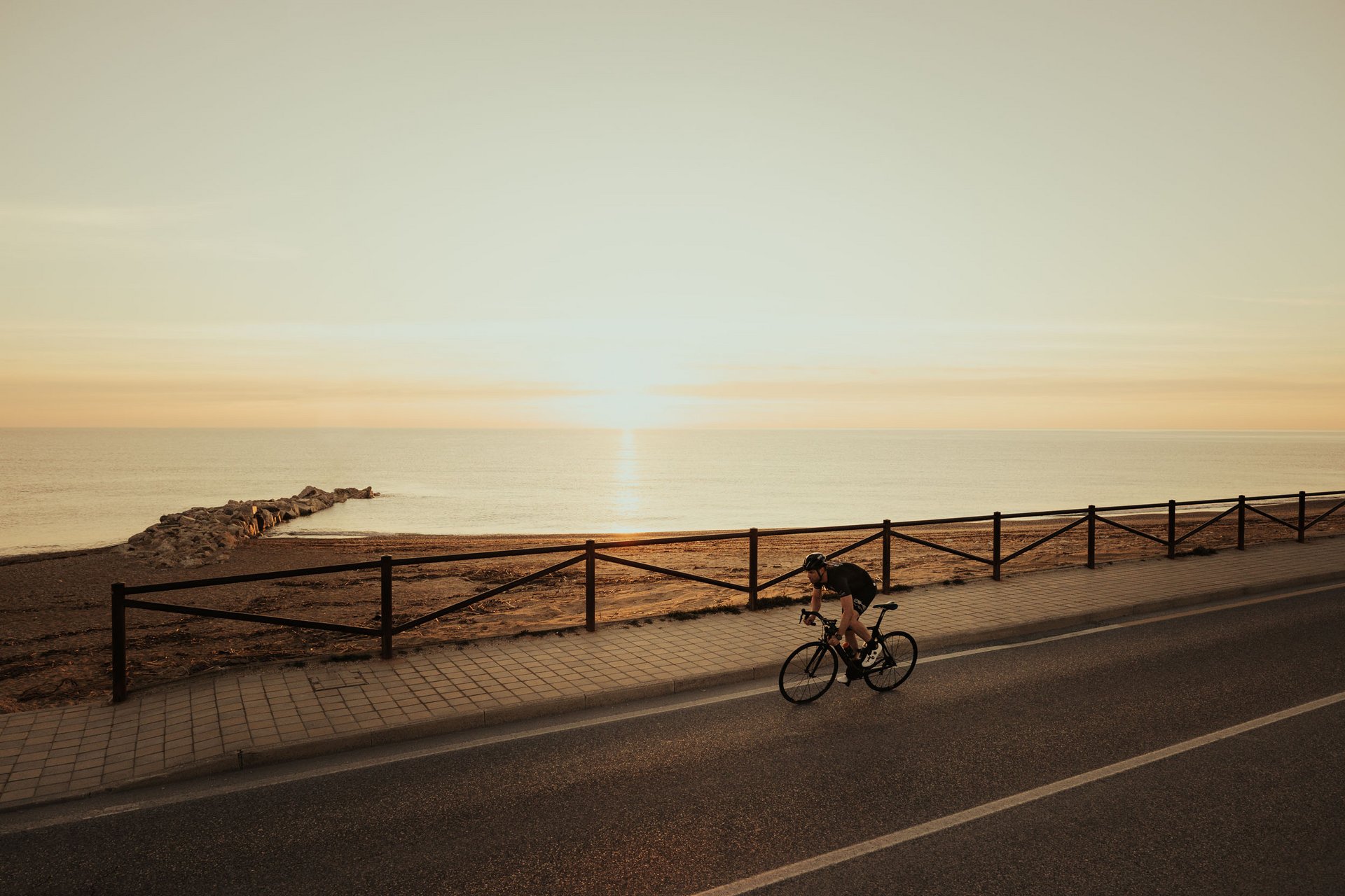 Ciclista che pedala lungo la strada vicino al mare al tramonto