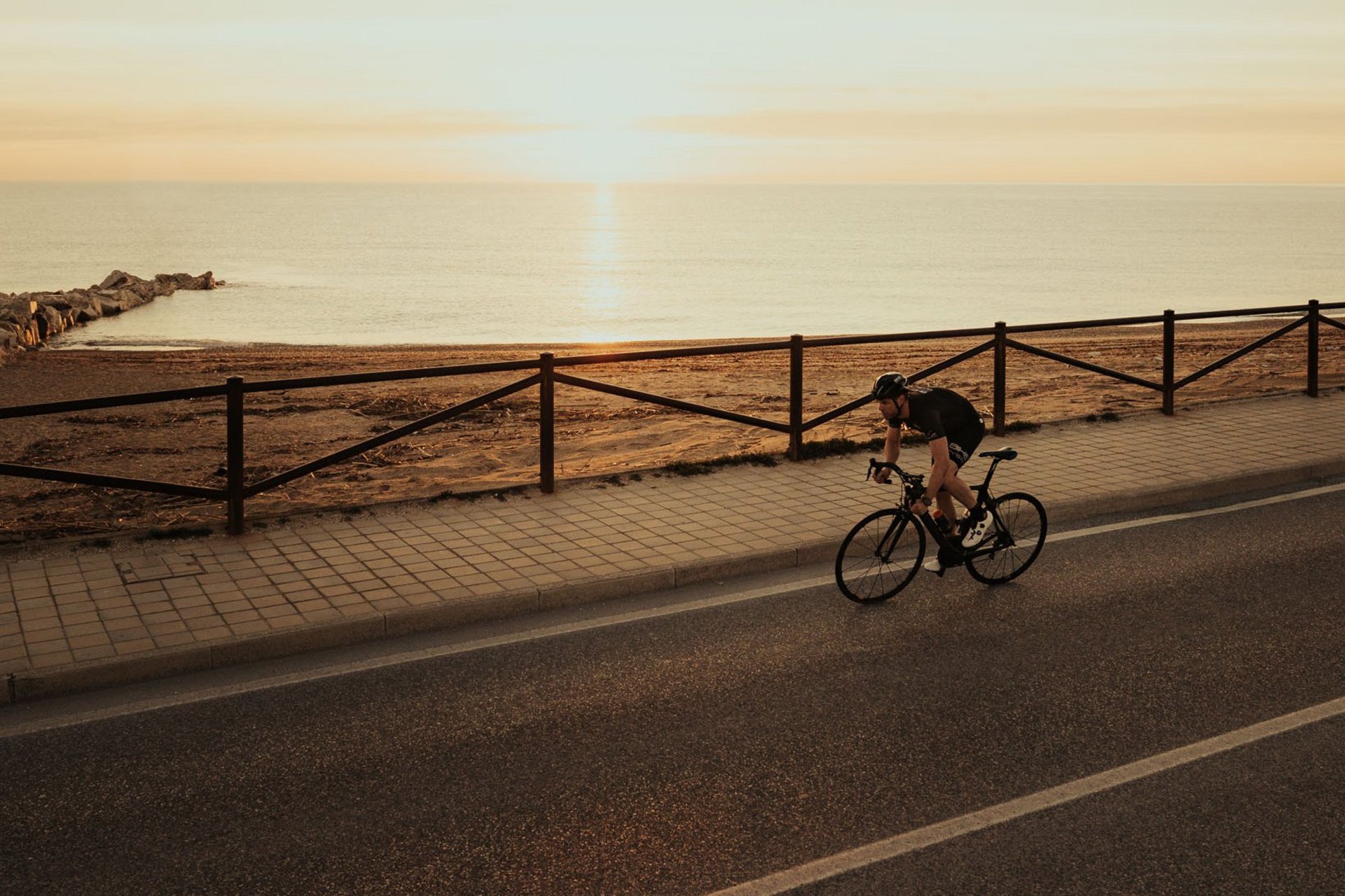 Radfahrer fährt am Meer entlang bei Sonnenuntergang