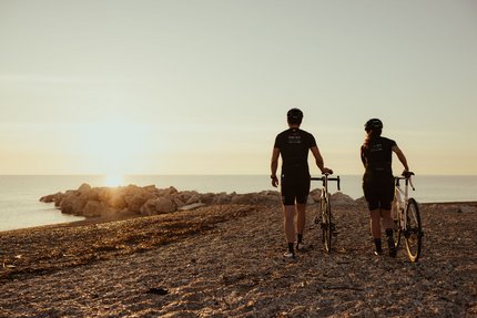 Zwei Radfahrer bei Sonnenuntergang am Strand mit Blick aufs Meer