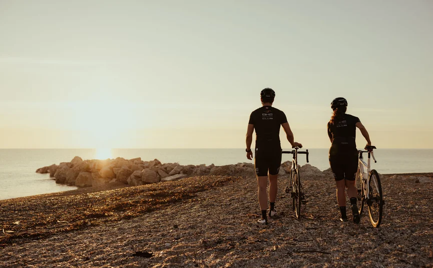 Zwei Radfahrer bei Sonnenuntergang am Strand mit Blick aufs Meer