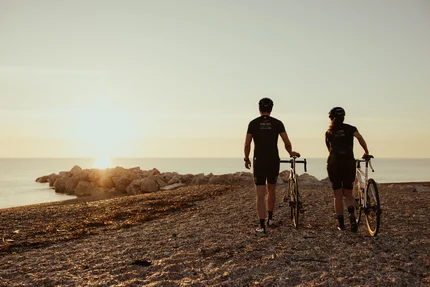 Zwei Radfahrer bei Sonnenuntergang am Strand mit Blick aufs Meer