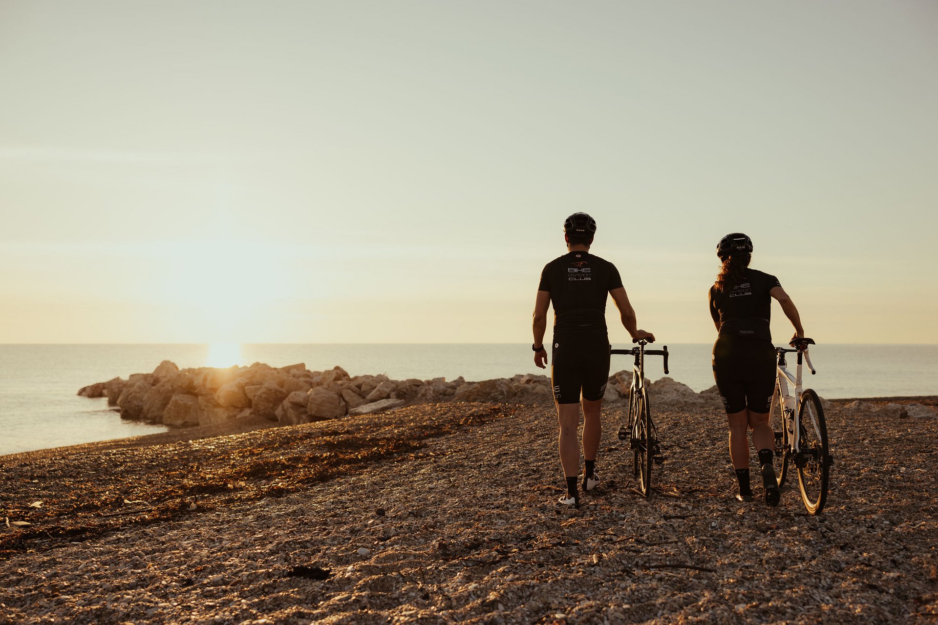 Zwei Radfahrer bei Sonnenuntergang am Strand mit Blick aufs Meer