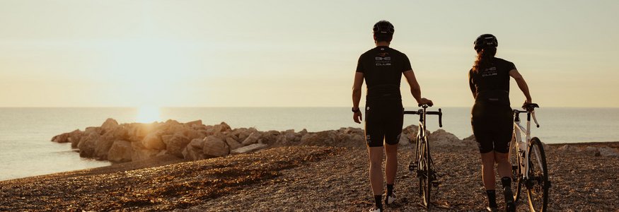 Zwei Radfahrer bei Sonnenuntergang am Strand mit Blick aufs Meer