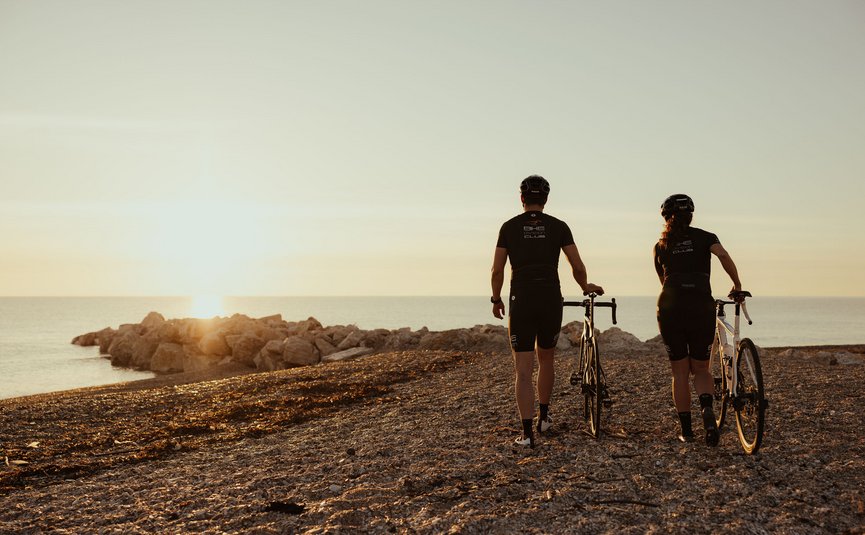 Due ciclisti che camminano sulla spiaggia al tramonto guardando il mare