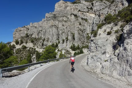 Cyclist riding a winding mountain road with rocky cliffs and blue sky