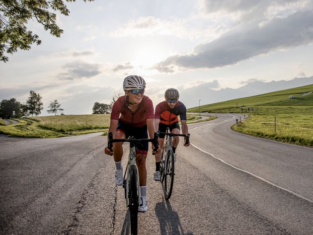 Zwei Radfahrer fahren auf einer Landstraße bei Sonnenuntergang