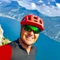Ciclista sorridente con casco rosso davanti a montagna e lago