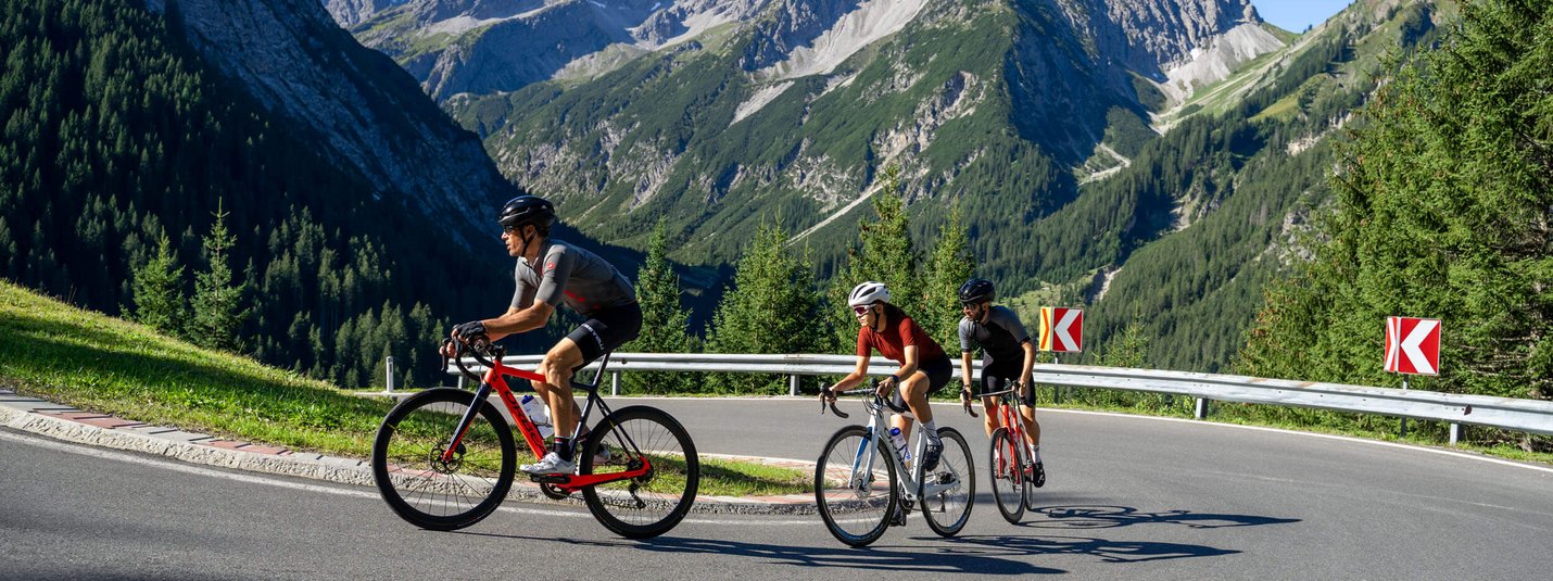 Drei Radfahrer fahren auf gebirgiger Straße mit klar blauem Himmel