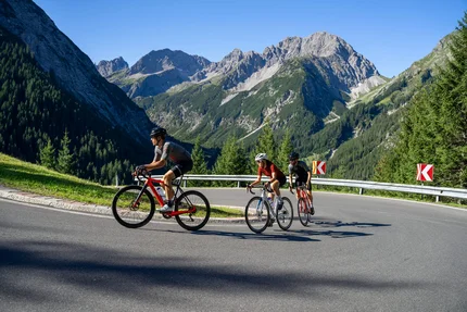 Drei Radfahrer fahren auf gebirgiger Straße mit klar blauem Himmel