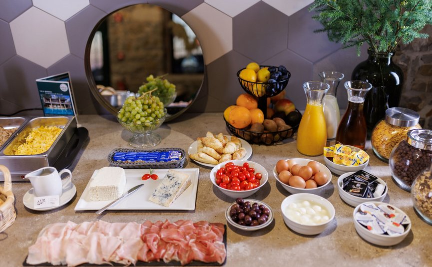 Buffet with cold cuts, cheese, eggs, fruits, and drinks on a gray countertop