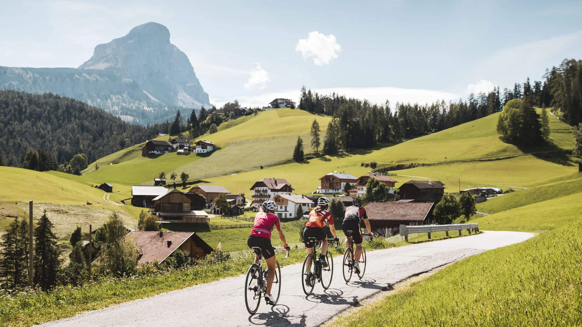 Goldene Kilometer: Rennrad-Herbst in San Vigilio © Alex Moling Drei Radfahrer fahren auf Landstraße im sonnigen Tal mit Berg im Hintergrund
