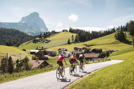 Drei Radfahrer fahren auf Landstraße im sonnigen Tal mit Berg im Hintergrund