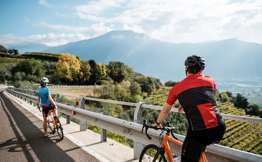Due ciclisti con casco su strada di montagna con vista su vallata e montagne
