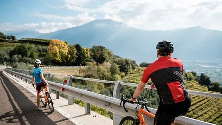 Zwischen Passstraßen, See & Dolce Vita beim Rennradurlaub am nördlichen Gardasee © Alex Moling Zwei Radfahrer mit Helmen auf Bergstraße mit Blick auf Tal und Berge