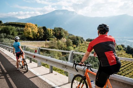 Due ciclisti con casco su strada di montagna con vista su vallata e montagne