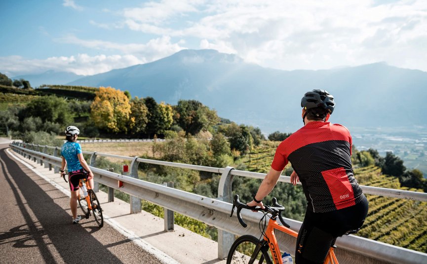 Due ciclisti con casco su strada di montagna con vista su vallata e montagne