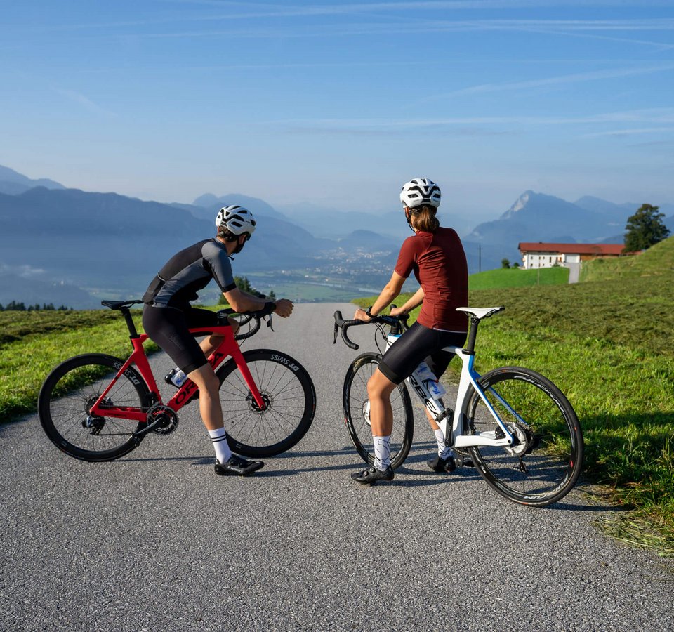 Kufsteinerland-Roadbike-Hotlist © Christina Neubauer Zwei Radfahrer auf Landstraße blicken auf Berglandschaft