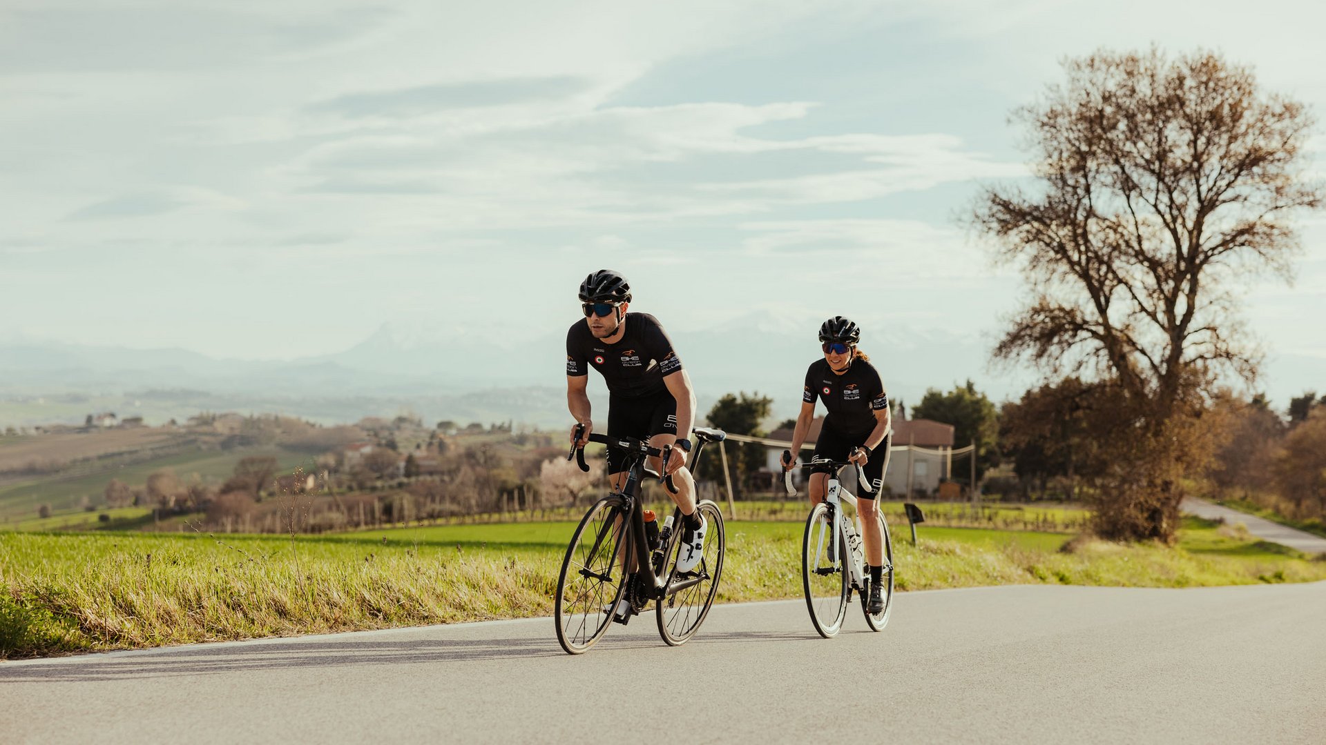 Zwei Radfahrer auf Landstraße mit grüner Landschaft und Baum