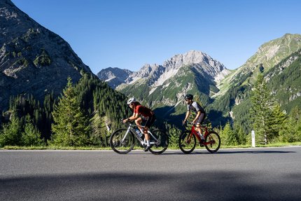 Zwei Radfahrer fahren auf Bergstraße mit Alpen im Hintergrund