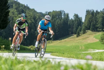 Due ciclisti pedalano su strada di campagna in paesaggio verde sotto il sole
